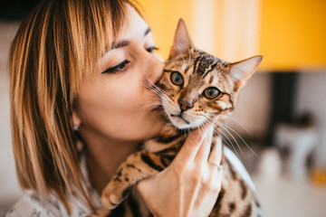 Blonde woman stands with Bengal cat in the yellow kitchen