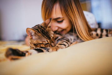 Woman leans to Bengal cat while it lies on bed