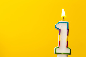 Number 1 birthday celebration candle against a bright yellow background