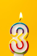 Number 3 birthday celebration candle against a bright yellow background