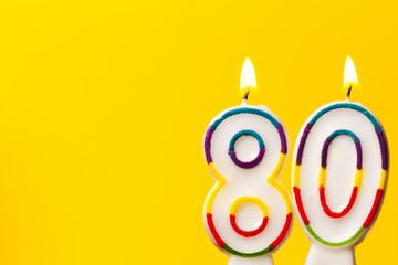Number 80 birthday celebration candle against a bright yellow background