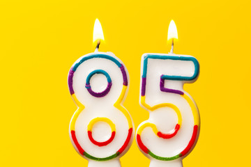 Number 85 birthday celebration candle against a bright yellow background