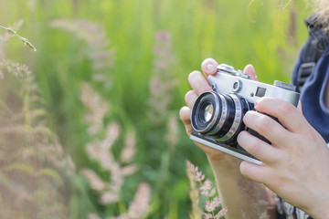 Hands of a girl holding a vintage camera on a background of high green grass