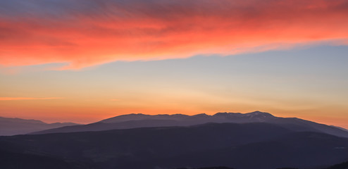 Fototapeta na wymiar Reddish sunrise with mountains and clouds. Atmospheric phenomena concept