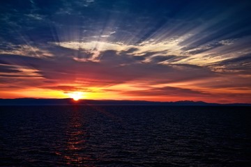 Beautiful sunrise in the ocean. Sun rays between sky clouds. Dramatic picture.