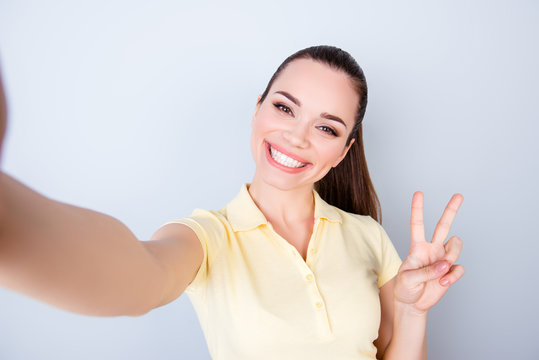 Cheers! Peace to all! Attractive young hispanic teen is making a selfie on the camera and shows two fingers sign, her smile is so beaming