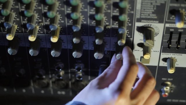 Cranking up the volume knob. Hands twist tumblers on control panel of guitar amplifier. Slowmotion.