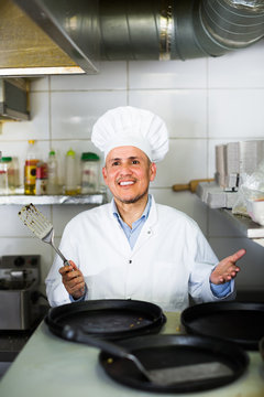 mature chef with frying pans in kitchen.