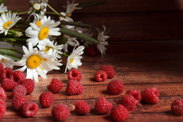 handful of ripe raspberries and chamomile flowers on a wooden board