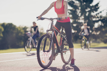 Cropped low angle photo of athletes cycling on the road outdoors, focused on a girl, she stopped, in trandy outfit, sneakers