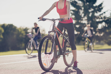 Fototapeta premium Cropped low angle photo of athletes cycling on the road outdoors, focused on a girl, she stopped, in trandy outfit, sneakers