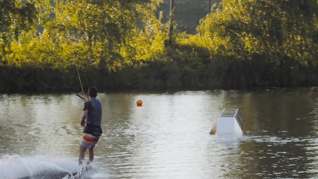 Wakeboarder ride on cable wakeboard in park, outdoor extreme slow motion on water, surfing athlete on water doing boardslide, noseslide or tailslide 180 out