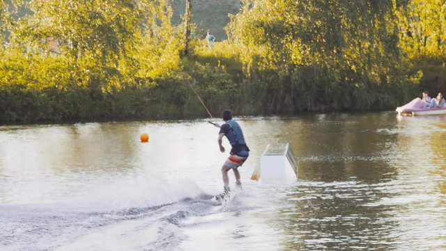 Wakeboarder ride on cable wakeboard in park, outdoor extreme slow motion on water, surfing athlete on water doing boardslide, noseslide or tailslide 180 out