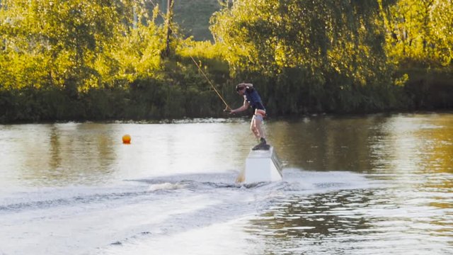 Wakeboarder ride on cable wakeboard in park, outdoor extreme slow motion on water, surfing athlete on water doing boardslide, noseslide or tailslide 180 out