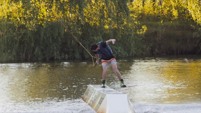 Wakeboarder ride on cable wakeboard in park, outdoor extreme slow motion on water, surfing athlete on water doing boardslide, noseslide or tailslide 180 out, backside bluntslide