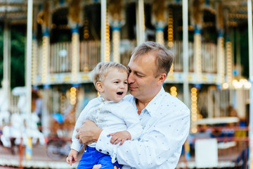 Father holding his crying son in front of carousel in amusement park