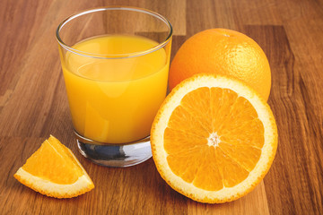 Fresh orange juice in the glass next to the orange slices on wooden table