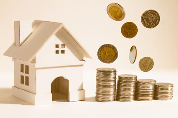 A home model and coin stack and dropping on paper background, the saving money for buying a new realty concept.