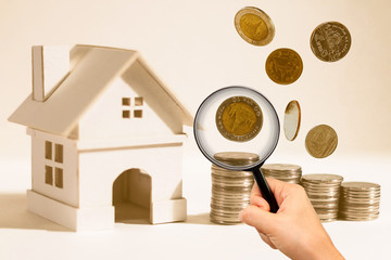 A magnifier and home model and coin stack/dropping on paper background, searching the saving money for buying a new realty concept.