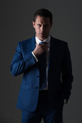 Successful man adjusting tie in stylish blue formal suit