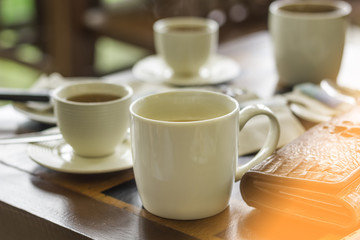 White coffee mug and white tea mug put on a brown wooden table in the morning cafe.