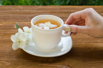 Female hand and a white mug of tea with jasmine on a wooden table. Close-up