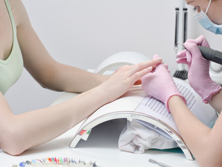 Girl in gloves handles nails with a milling cutter for manicure