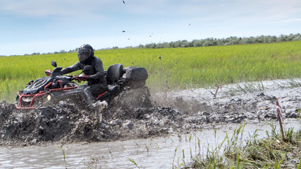 man in a helmet riding a quad in a muddy puddle