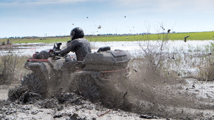 man in a helmet riding a quad in a muddy puddle
