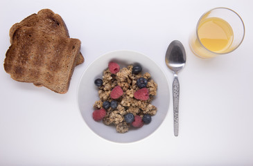 Bowl of fruit granola with orange juice and two slices of toast 