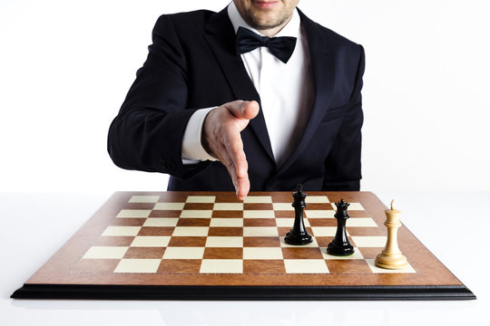 Game over. Smart man in a dark suit playing blacks has just won a game of 
chess and is about to give handshake.