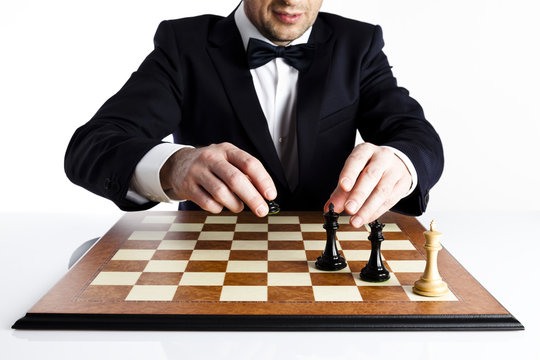 mart man in a dark suit playing whites chess is about to give checkmate to 
black king.