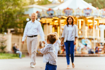 Mignon petit garçon courant dans un parc d& 39 attractions avec sa famille en arrière-plan. Concept de vacances en famille.
