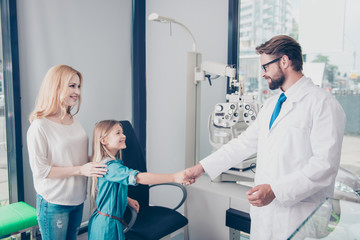 Small cute patient is saying thank you and bye to the friendly bearded brunet male optician, mom is...