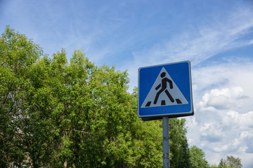 Pedestrian crossing sign with a blue sky and green trees on background