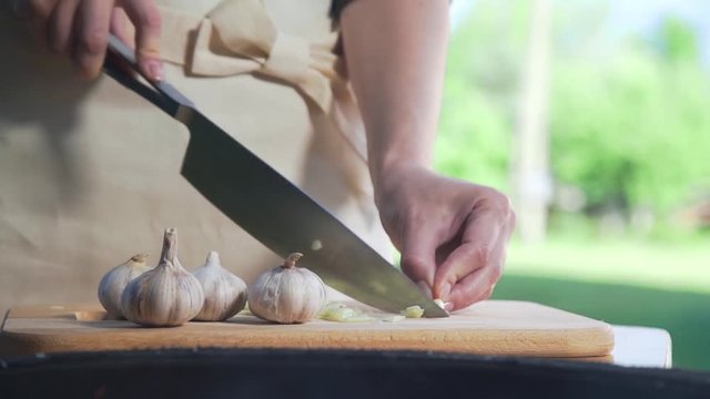Chef shreds garlic on the wooden board near the grill's fire, makinf of salad, vegetable meal, vitamins in daily food, cooking outdoors
