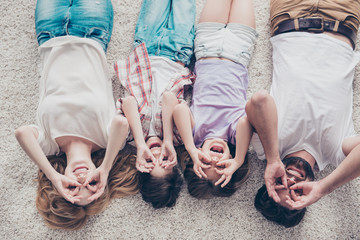 High angle view of happy family of four is joking, lying on the beige cozy carpet in a row, at...