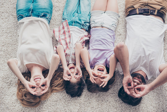 High Angle View Of Happy Family Of Four Is Joking, Lying On The Beige Cozy Carpet In A Row, At Home, All Cheerful, Smiling, Gesturing