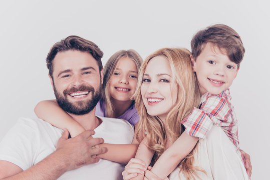 Family photo portrait. Four relatives are hugging on the white background, smiling, at home, blond mum is piggy backing the cute small son