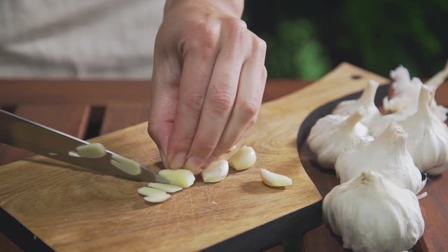 Chef shreds garlic on the wooden board near the grill's fire, makinf the salad, vegetable meal, vitamins in daily food, cooking outdoors