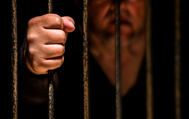 ein Mann ist im Gefängnis eingesperrt, seine Faust umschlingt das Gitter der Gefängniszelle