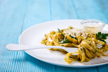 Fetuchini Pasta with sauce. Hot dish with Parmesan cheese, decorated with green parsley on a blue background.Copy space for Text.selective focus.