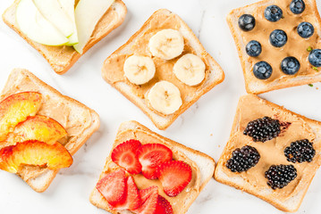 Traditional American and European summer breakfast: sandwiches of toast with peanut butter, berry, fruit apple, peach, blueberry, blueberry, strawberry, banana. White marble table. copy space top view