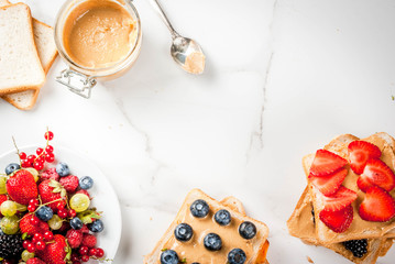 Traditional American and European summer breakfast: sandwiches of toast with peanut butter, berry, fruit apple, peach, blueberry, blueberry, strawberry, banana. White marble table. copy space top view