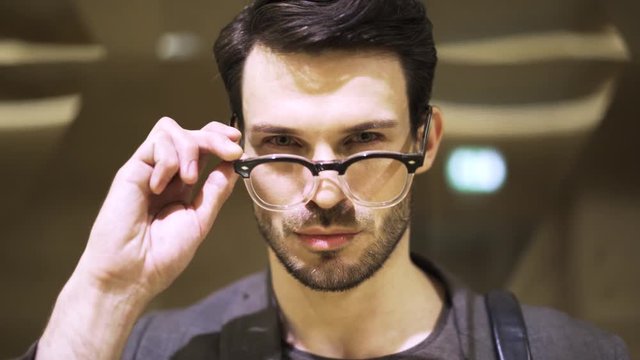 Handsome and young businessman in glasses walking to the camera, moving his glasses and looking at the viewer. Locked down real time close up shot