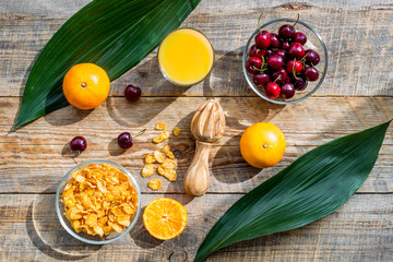 Preparing healthy summer breakfast. Muesli, oranges, cherry, juice on wooden table background top view