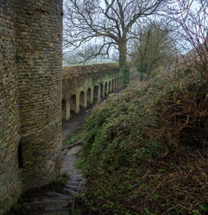 Naklejka premium The old fortress wall and a fragment of the tower, green with time. City of Berg, France. In the foreground is a overgrown hillside and a stone staircase.