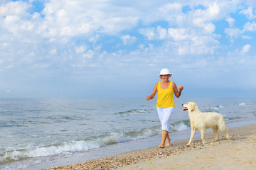 Happy elderly woman walking along a beach with her golden retriever at the morning