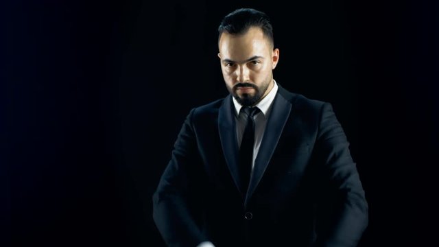 Professional Magician in a Dark Suit Creates Spectacular Illusion Where White Shawl Turns into White Parrot. Shot with Black Background. Shot on RED EPIC-W 8K Helium Cinema Camera.