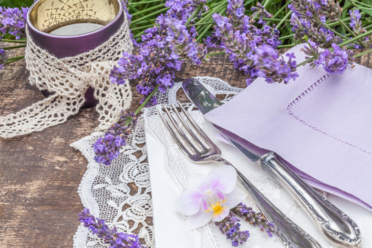 Tischdekoration mit Gedeck auf alter Holzplatte im Garten mit viel Lavendel